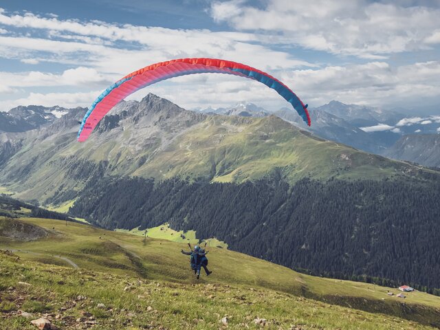 Abheben beim Gleitschirmflug auf dem Jakobshorn | © Davos Klosters Mountains Der Gleitschirm hebt ab und die beiden Passagiere fliegen bei einem Tandemflug hinunter nach Davos. | © Davos Klosters Mountains