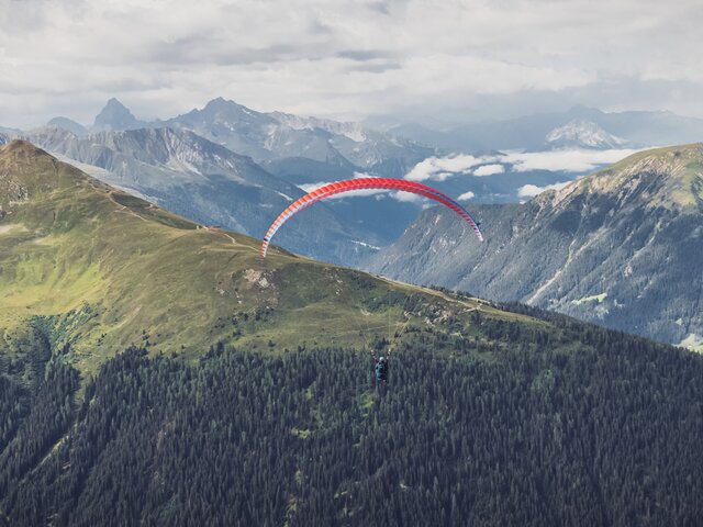 Gleitschirmflug in Richtung Horizont | © Davos Klosters Mountains Der rote Gleitschirm fliegt zum Horizont in Richtung Rinerhorn. | © Davos Klosters Mountains