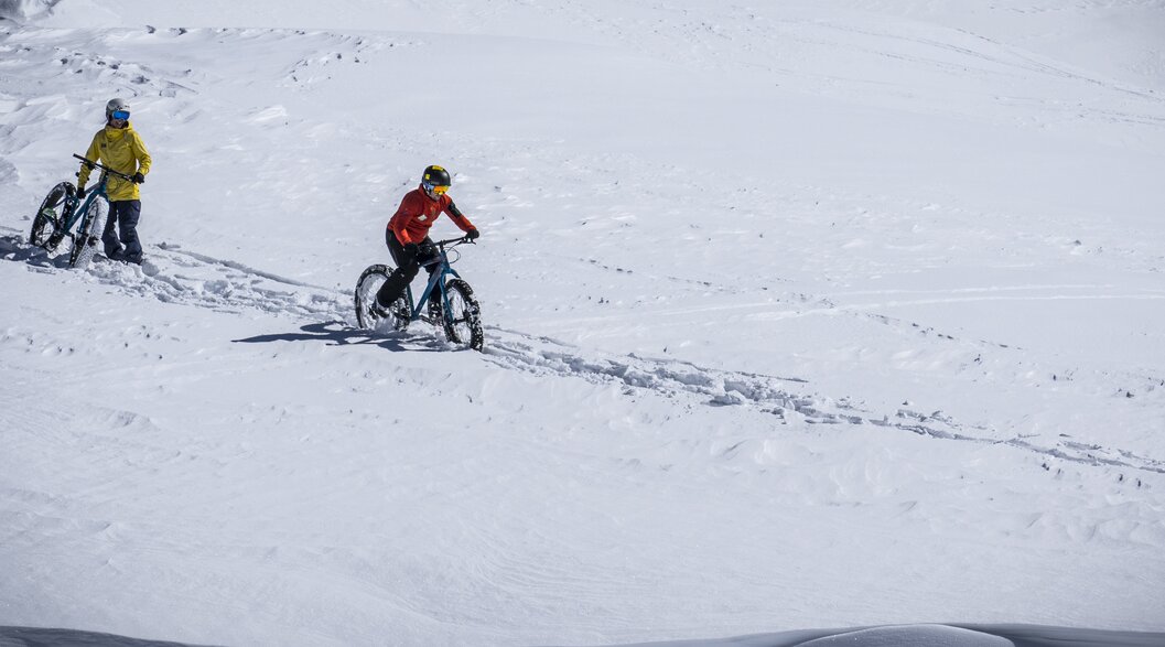 Mann und Frau fahren mit Ihren Fatbikes im Tiefschnee den Berg hinunter. | © Davos Klosters Mountains