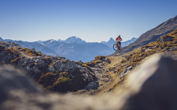 Ein Biker macht einen Sprung auf dem Signaltrail auf Gotschna, das Tinzenhorn im Hintergrund.  | © Davos Klosters Mountians