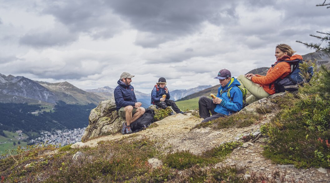 Eine vierköpfige Familie legt auf Ihrer Wanderung auf dem Rinerhorn eine Pause ein und hat sich für die Stärkung einen Platz mit Blick nach Davos ausgesucht.  | © Davos Klosters Mountains