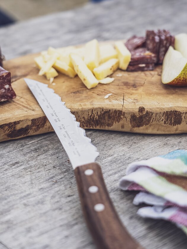 Auf einem Holzbrett sind Wurst, Käse und Obstscheiben aufgeschnitten als Stärkung auf der Wanderung. | © Davos Klosters Mountains