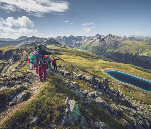 Eine Gruppe von Wanderer blickt vom Grat hinab auf den tiefblauen Stadlersee. | © Davos Klosters Mountains