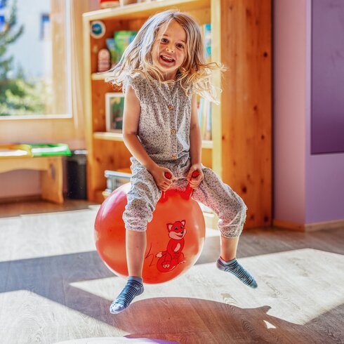 Ein Mädchen sitzt auf einem roten Ball und hüpft durch den Globi Kids Club im Hotel Waldhuus Davos. | © DDO - davos.ch | Martin Bissig